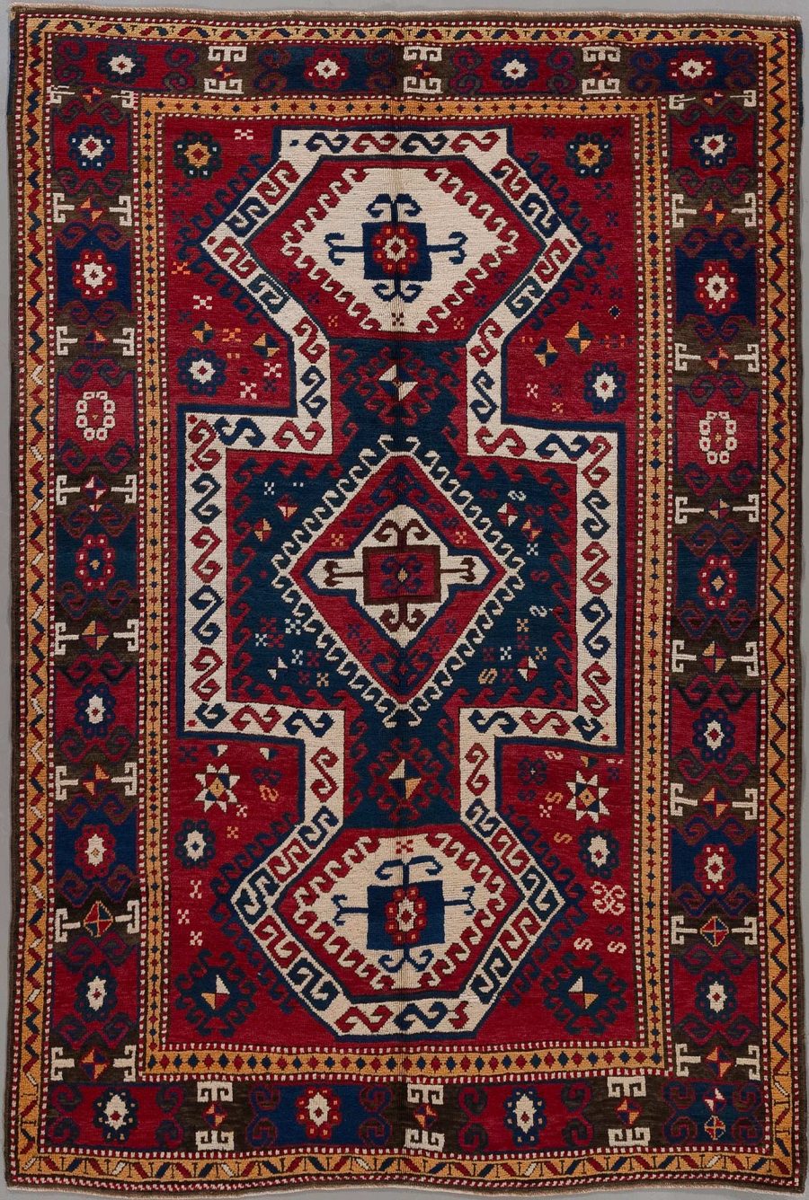 Traditioneller handgeknüpfter Teppich mit komplexem Muster, bestehend aus geometrischen Formen und symbolischen Motiven in Farben von Rot, Blau, Beige und einigen Akzenten in Dunkelblau und Weiß.