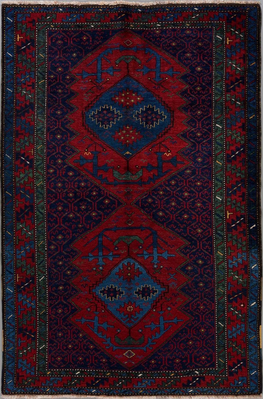 Traditioneller handgeknüpfter Teppich mit komplexem, symmetrischem Muster in Rot- und Blautönen mit Akzenten in Grün und Weiß. Zwei dominante, zentrale Rhombus-Formen umgeben von detaillierten Bordüren.