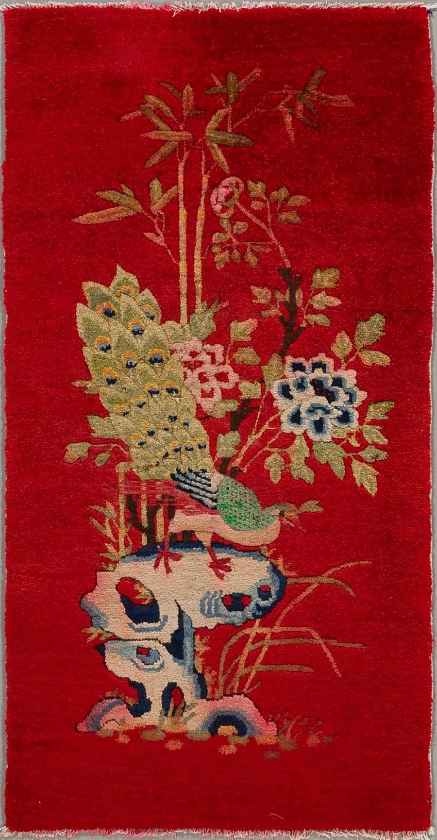 Handgeknüpfter Wandteppich mit floralem Muster auf rotem Hintergrund, der eine stilisierte Landschaft mit verschiedenen Pflanzen und einem Vogel zeigt.