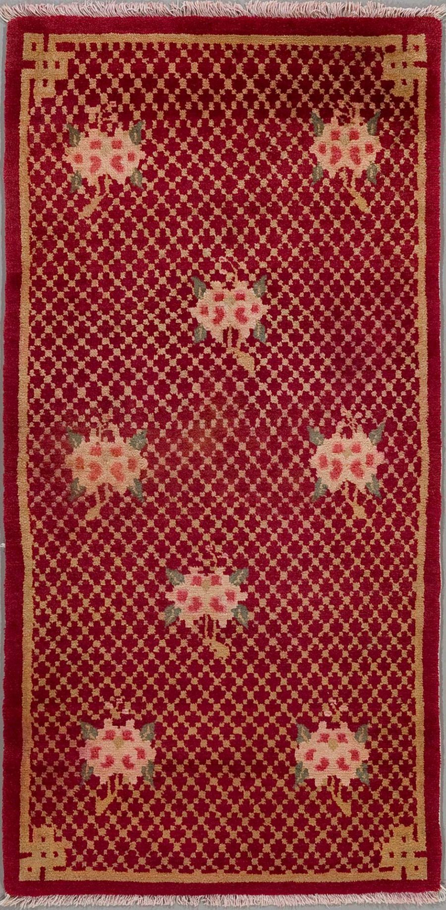 Langlicher, orientalischer Teppich mit rotem Hintergrund und kleinen wiederholenden Mustern; mit größeren, floralen Motiven und einer einfachen Bordüre in Beige und Weinrot. Fransen an den schmalen Enden.