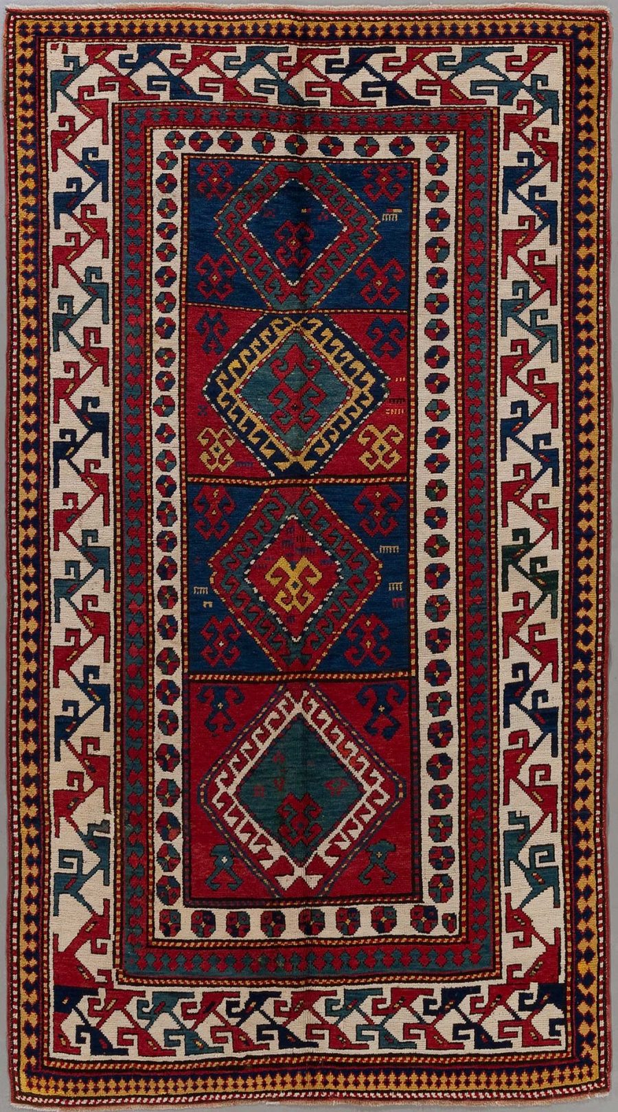 Traditioneller handgewebter Teppich mit komplexen geometrischen Mustern und Bordüren in Farben wie Dunkelblau, Rot, Beige und Akzenten in Grün und Gelb.