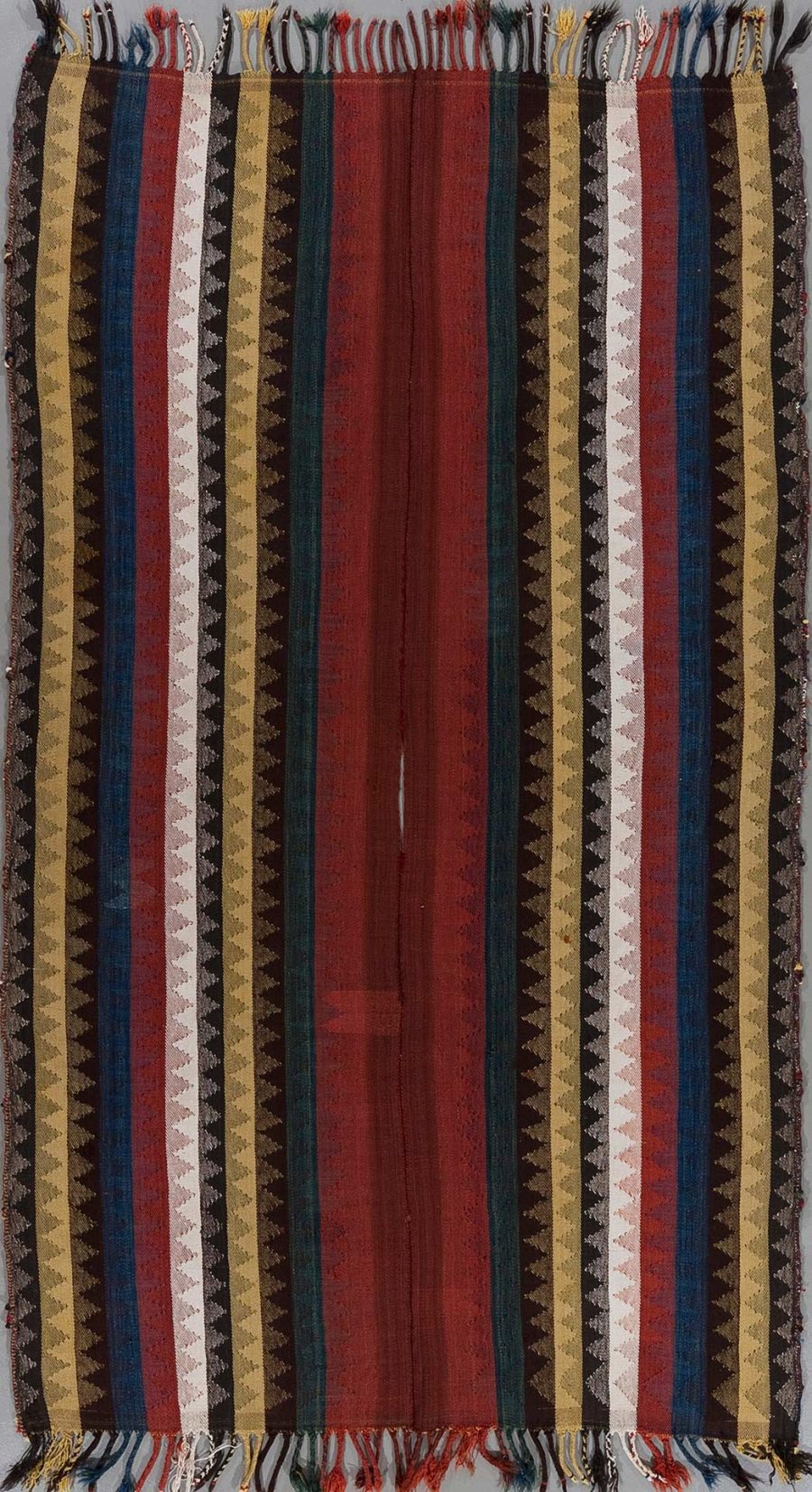 Traditioneller gewebter Textilvorhang mit vertikalen Streifenmuster in diversen Farben wie Rot, Blau, Braun und Creme, verziert mit Zacken- und Rautenmustern, und Fransen an den Enden.