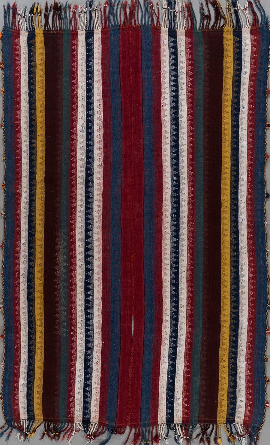 Handgewebter Teppich mit vertikalen Streifen in verschiedenen Farben wie Rot, Blau, Gelb und Grün sowie eingearbeiteten Mustern, hängend mit Fransen an beiden Enden.