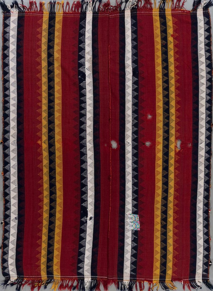 Gewebter Wandteppich mit vertikalen Streifen in Rot, Gelb und Schwarz, mit hängenden Fransen an der Unterkante und vereinzelten Gebrauchsspuren.