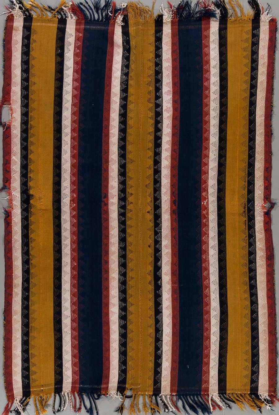 Farbenfrohes, gestreiftes Textil mit vertikalen Streifen in Blau, Rot, Gold und Beige, das an den Rändern ausgefranst ist.