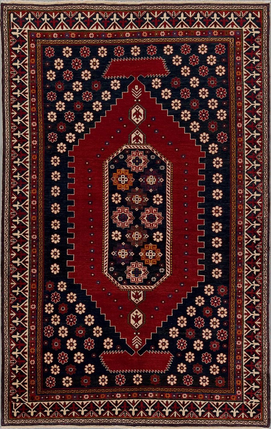 Traditioneller handgeknüpfter Teppich mit kompliziertem Muster, das hauptsächlich in Rottönen mit Akzenten in Blau, Weiß und Gold gehalten ist, umrahmt von mehreren dekorativen Bordüren.