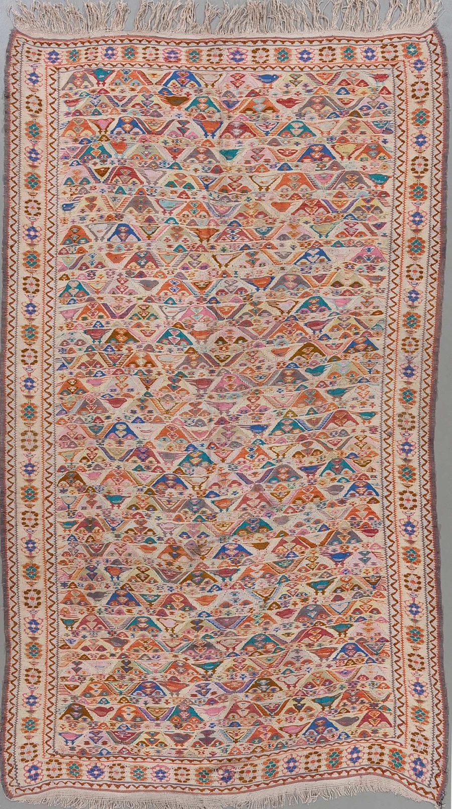 Handgewebter Teppich mit komplexem, geometrischem Muster und vielfältiger Farbpalette, umrahmt von dekorativen Bordüren und versehen mit Fransen an den kurzen Enden.