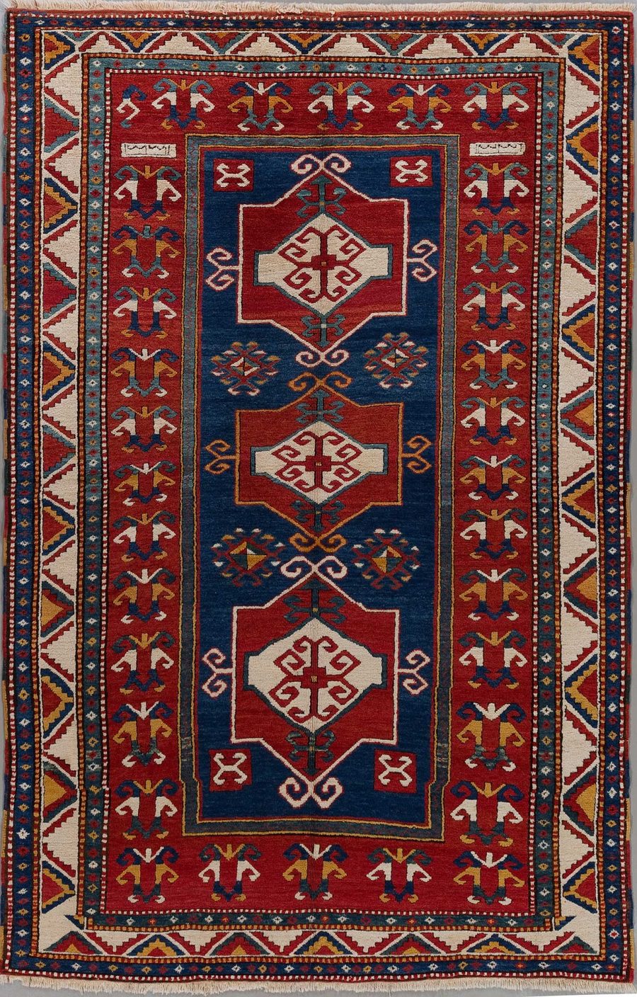 Handgeknüpfter orientalischer Teppich mit detailliertem Muster, dominierenden Farben in Dunkelblau und Rot, umrandet von einem dekorativen Bordüren-Design und mehreren zentralen geometrischen Motiven.