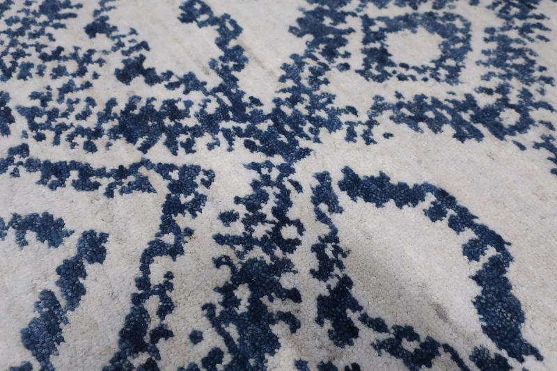 Nahaufnahme eines Teppichs mit traditionellem blauem Ornamentmuster auf cremeweißem Hintergrund.