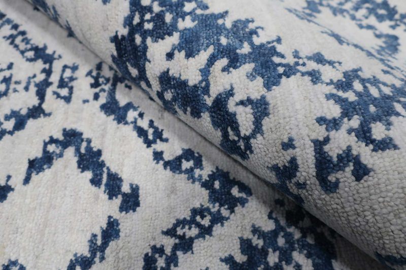 Nahaufnahme eines Teppichs mit traditionellem blauem Ornamentmuster auf cremeweißem Hintergrund.