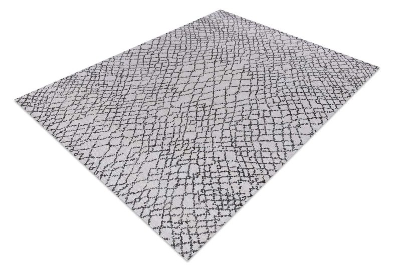 Rechteckiger Teppich mit einem abstrakt krakelierten Muster in Schwarz und Grau auf hellem Untergrund, aus der Vogelperspektive fotografiert.