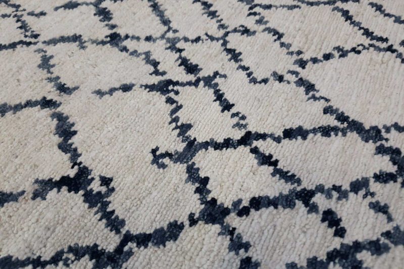 Nahaufnahme eines strukturierten Teppichs mit beige Hintergrund und wiederholendem, diamantförmigem dunkelblauem Muster.