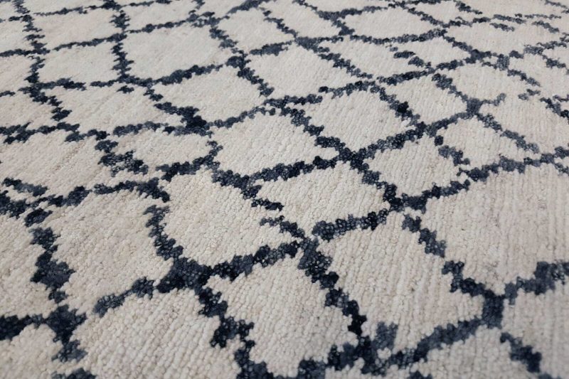 Nahaufnahme eines strukturierten Teppichs mit beige Hintergrund und wiederholendem, diamantförmigem dunkelblauem Muster.