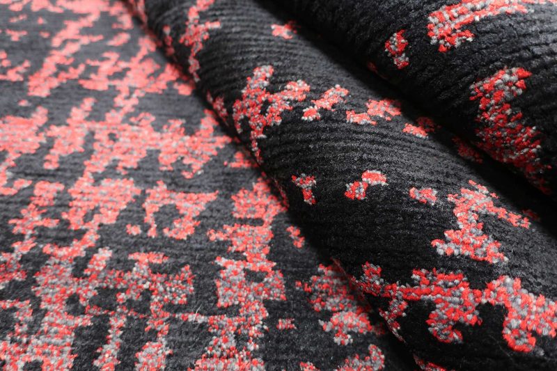 Nahaufnahme eines gemusterten Stoffes, vorwiegend in Schwarz mit einem abstrakten, pixeligen Muster in Rottönen.