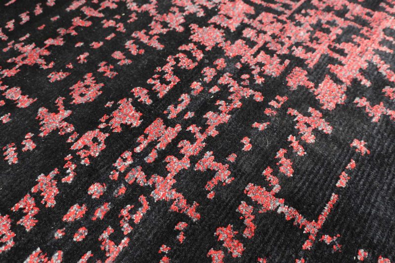 Nahaufnahme eines gemusterten Stoffes, vorwiegend in Schwarz mit einem abstrakten, pixeligen Muster in Rottönen.