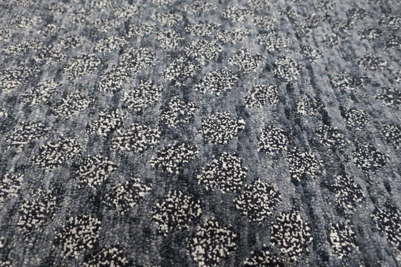 Nahaufnahme eines strukturierten, dunkelgrauen Teppichs mit eingewebten weißen Sprenkeln, die ein unregelmäßiges Muster bilden.