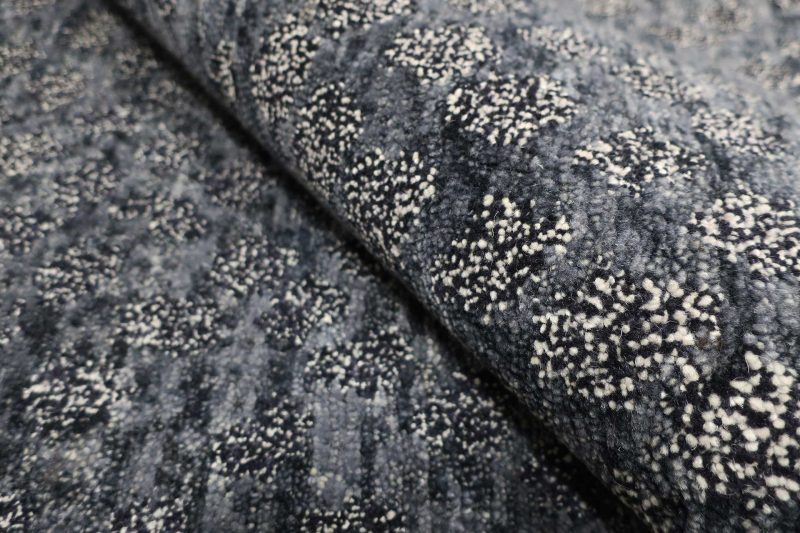 Nahaufnahme eines strukturierten, dunkelgrauen Teppichs mit eingewebten weißen Sprenkeln, die ein unregelmäßiges Muster bilden.