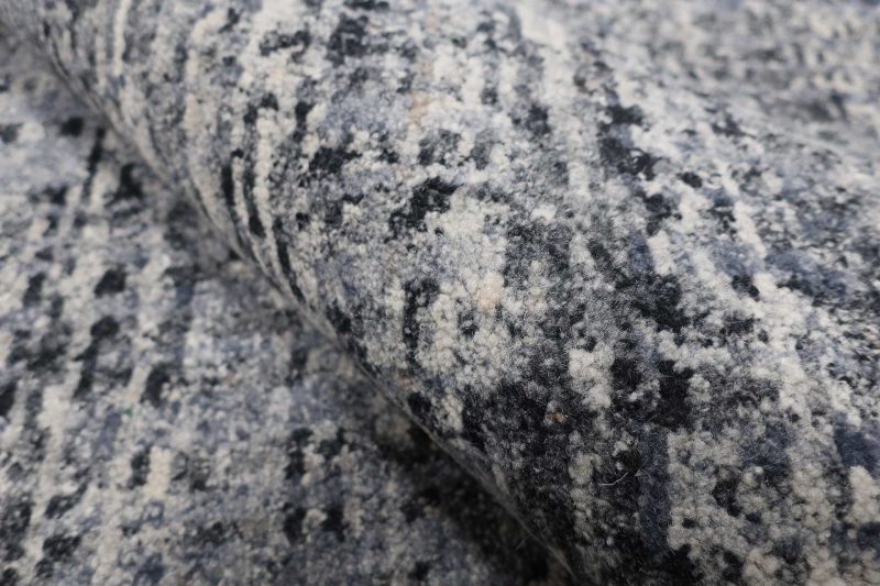 Strukturierte Nahaufnahme eines gemusterten Teppichs mit grau-schwarzen und weißen Farbnuancen.