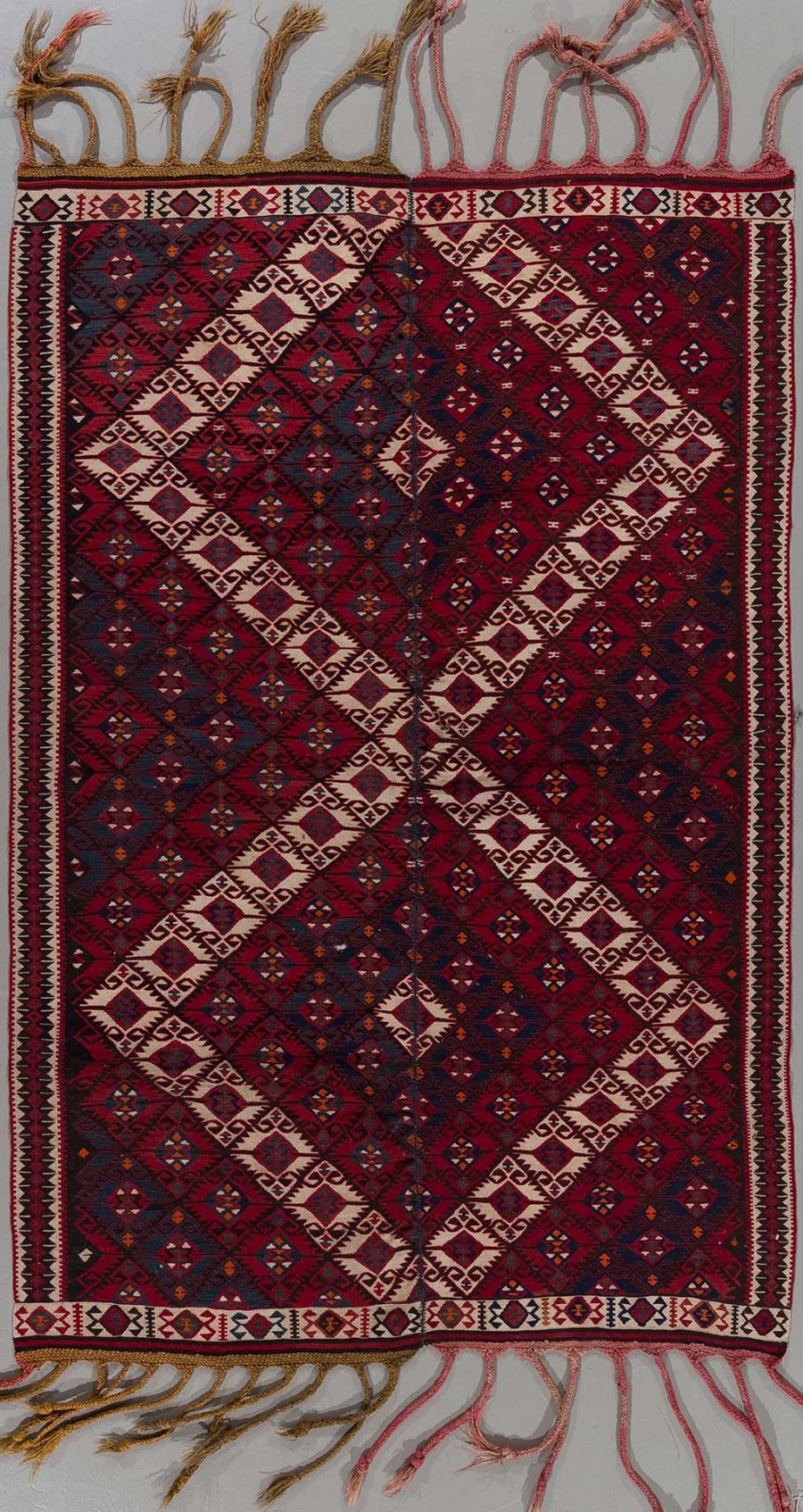 Traditioneller Teppich mit komplexem, geometrischem Muster in überwiegend roten und blauen Farbtönen, umrahmt von einer dekorativen Bordüre und ausgefransten Enden.