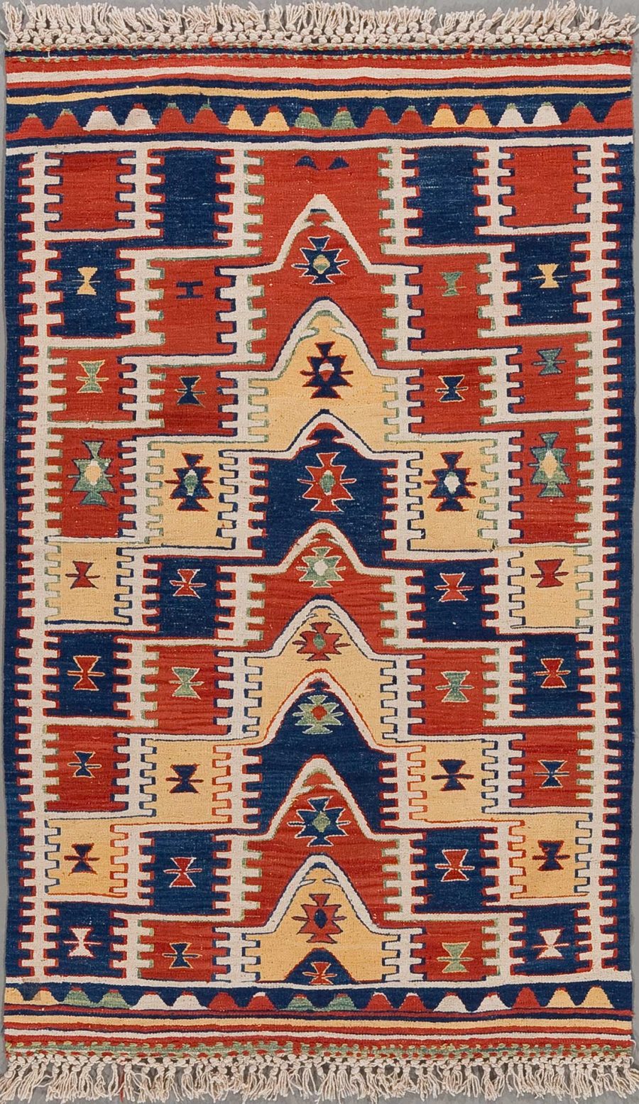 Detailreich gewebter Teppich mit traditionellen Mustern in den Farben Rot, Blau, Beige und Akzenten in Orange und Grün, umgeben von einer Bordüre mit geometrischen Formen und abgeschlossen mit Fransen an beiden Enden.