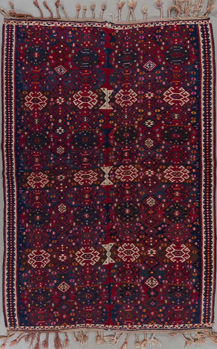Traditioneller handgeknüpfter Teppich mit komplexem geometrischem Muster und reichen Farben, hauptsächlich in Dunkelblau und Rot, mit Details in Beige, Rosa und anderen Farben, umrahmt von mehreren Bordüren und Fransen an beiden Enden.