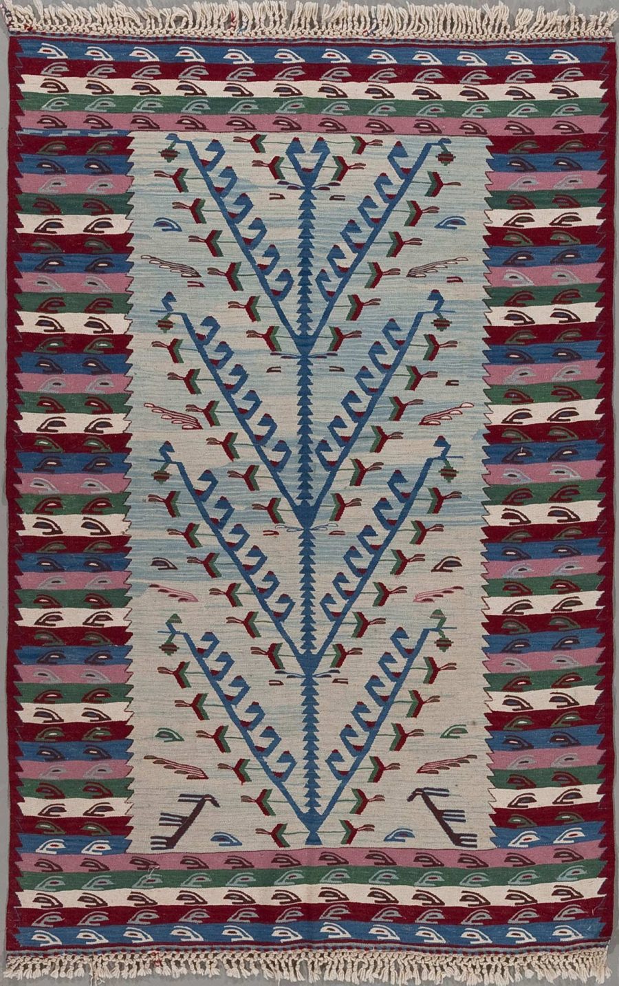 Handgewebter Teppich mit traditionellem geometrischem Muster in Blau, Rot, Grün und Beige, umrahmt von einer dekorativen Grenze und Fransen an den kurzen Seiten.