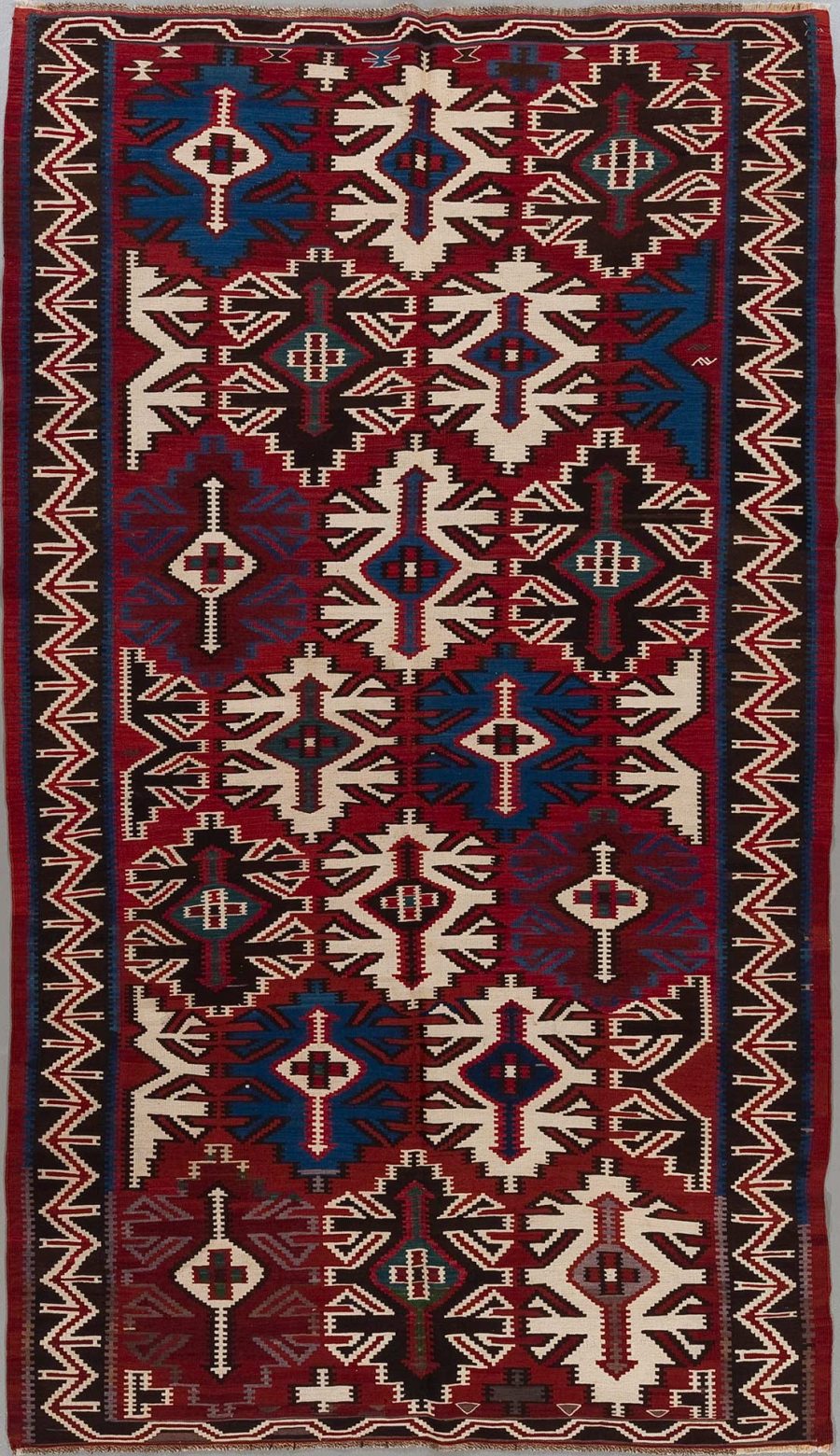 Traditioneller handgewebter Teppich mit komplexen geometrischen Mustern und Symmetrien, hauptsächlich in den Farben Rot, Blau, Schwarz und Weiß.