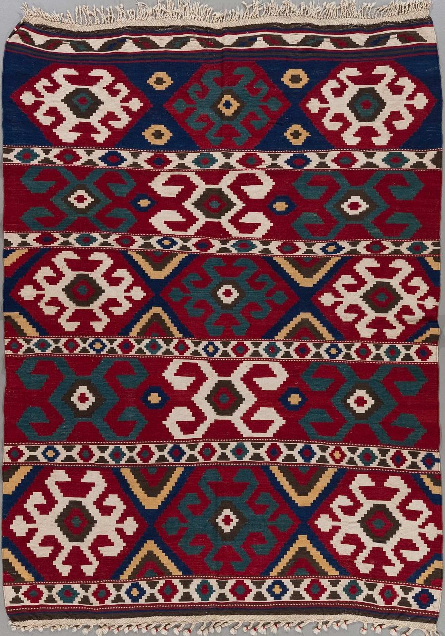 Handgewebter Teppich mit traditionellen Mustern in den Farben Rot, Blau, Weiß und Beige, mit Fransen an einem Ende.