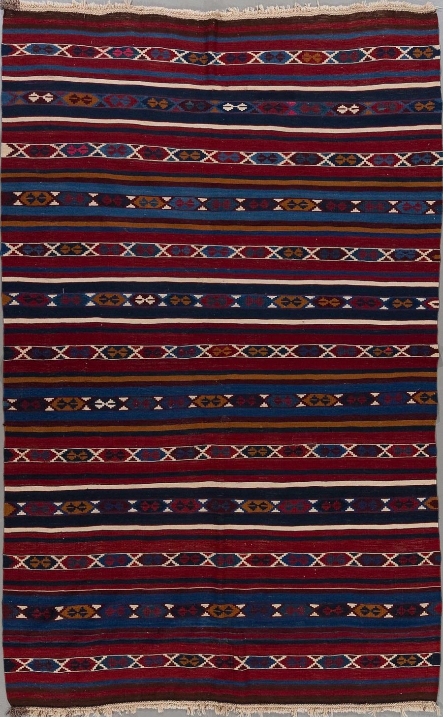 Handgewebter Teppich mit traditionellen Mustern in Farbtönen von Blau, Rot, Weiß und Gelb auf vertikalen Streifen.
