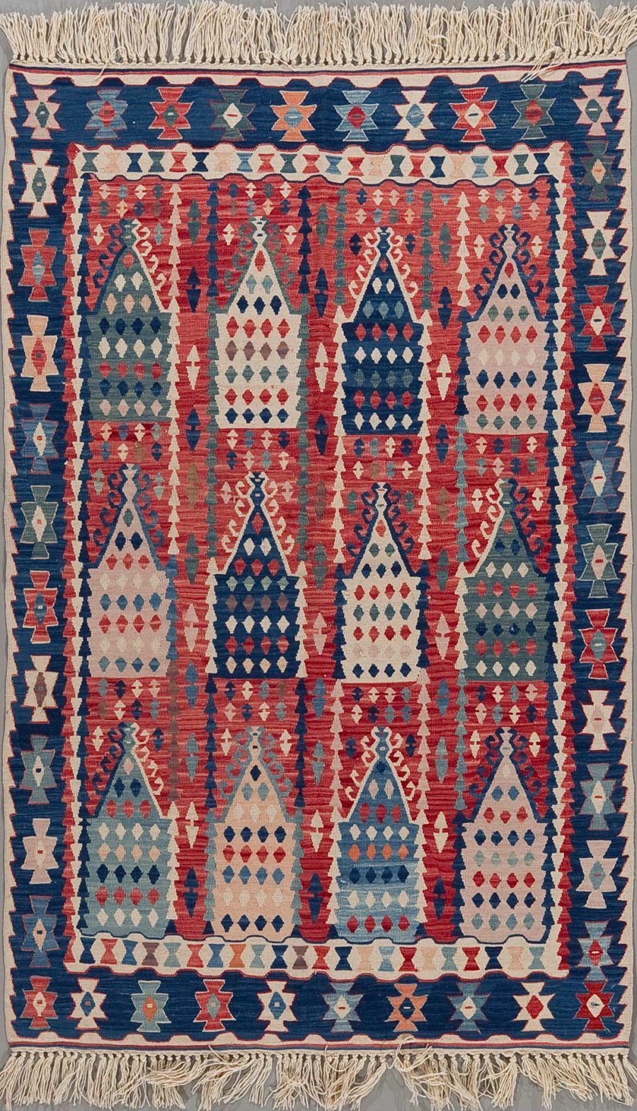 Traditioneller handgewebter Teppich mit komplexem geometrischem Muster in Rot-, Blau-, Weiß- und Beigetönen mit Fransen an den Enden.