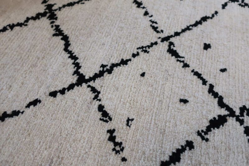 Nahaufnahme eines flauschigen, cremefarbenen Teppichs mit geometrischem Muster in Schwarz.