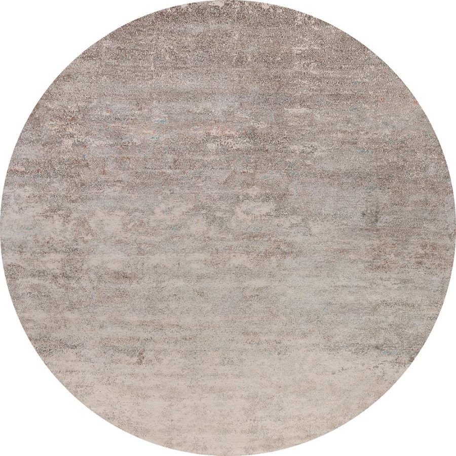 Runder Teppich mit abgenutzter Textur in verschiedenen Grau- und Beigetönen mit vereinzelten bläulichen Flecken.