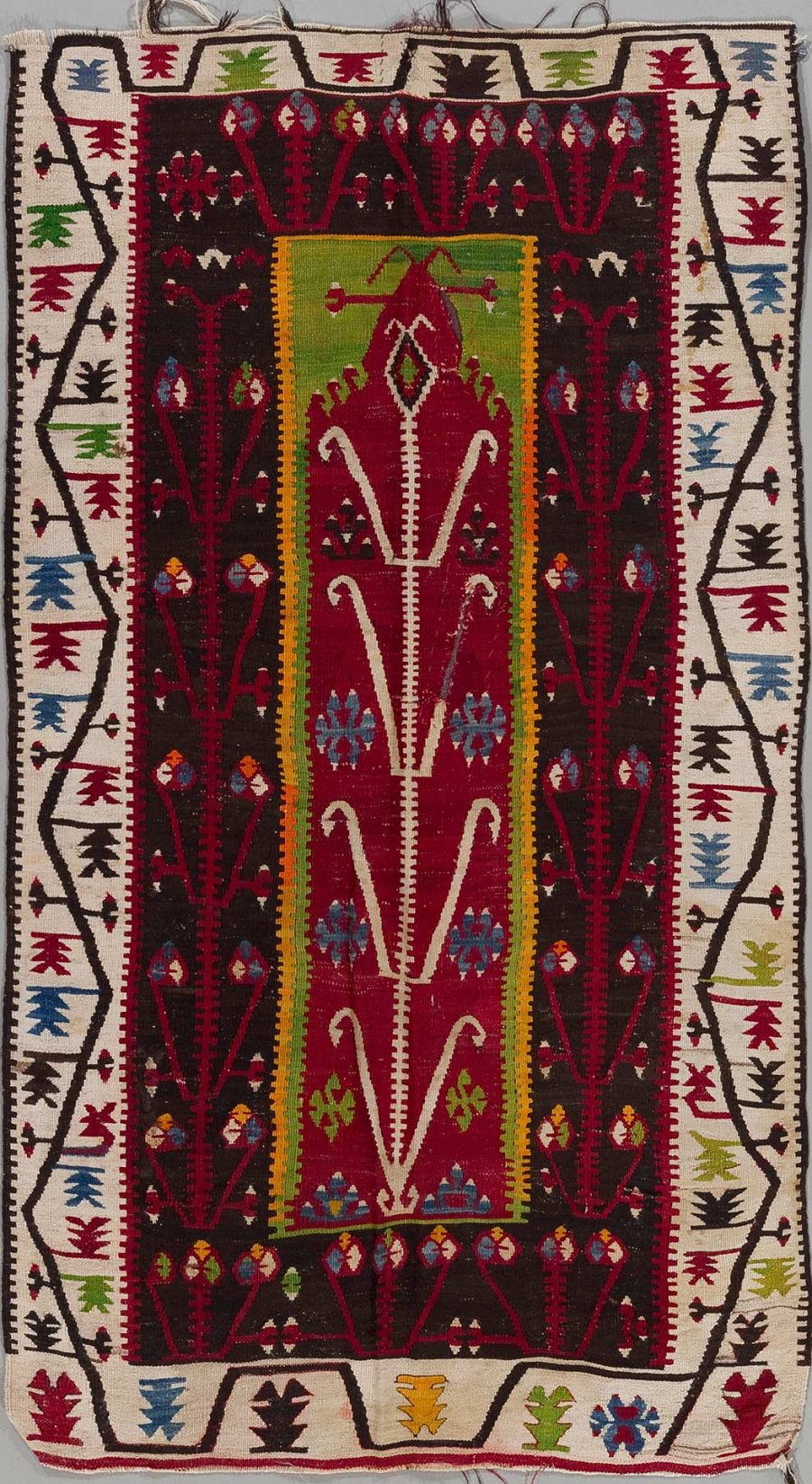 Handgewebter Teppich mit zentralem roten Feld, umgeben von mehrfarbigen geometrischen und floralen Mustern auf dunklem Hintergrund, mit Bordüren in Gelb, Weiß und Schwarz.