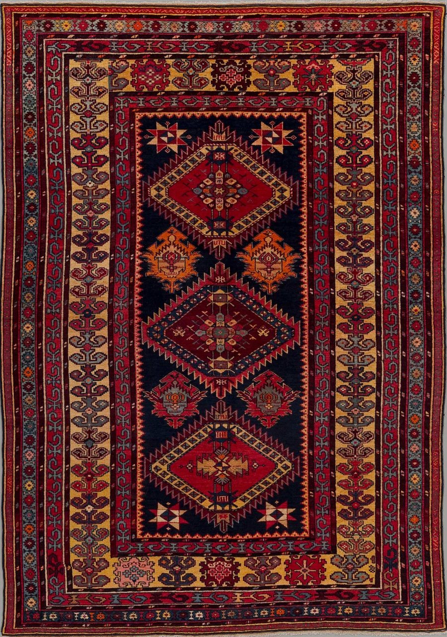 Ein traditioneller handgeknüpfter Teppich mit einem komplexen Muster, das hauptsächlich in dunklen Farbtönen gehalten ist, mit zentralen geometrischen Medaillons in Rot, Orange und Beige sowie umrahmenden dekorativen Bordüren in verschiedenen Mustern und Farben.