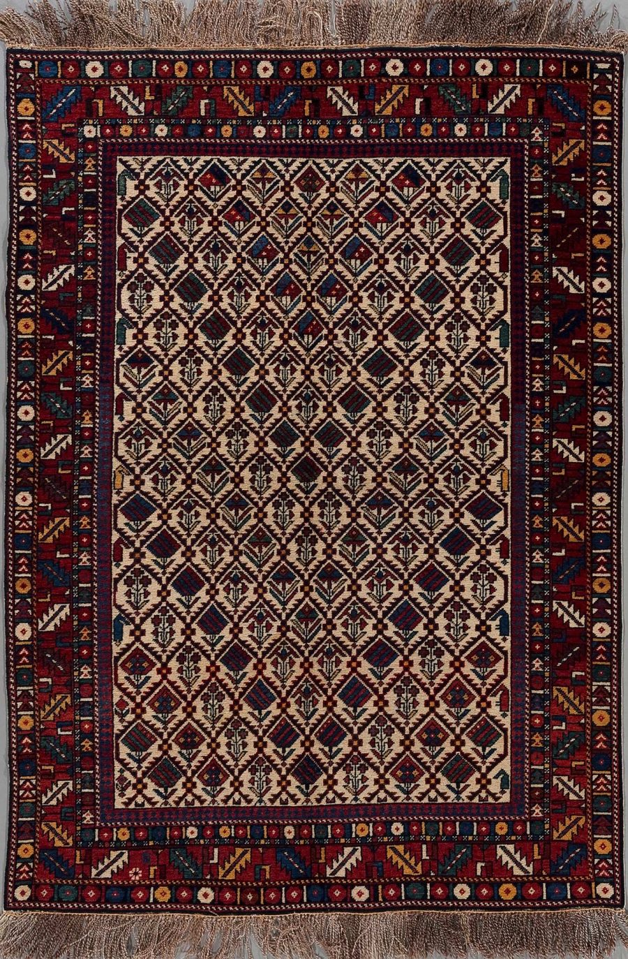 Traditioneller handgeknüpfter Teppich mit komplexen Mustern in warmen Rottönen sowie Blau-, Creme- und Brauntönen, aufgehängt vor einem neutralen Hintergrund.