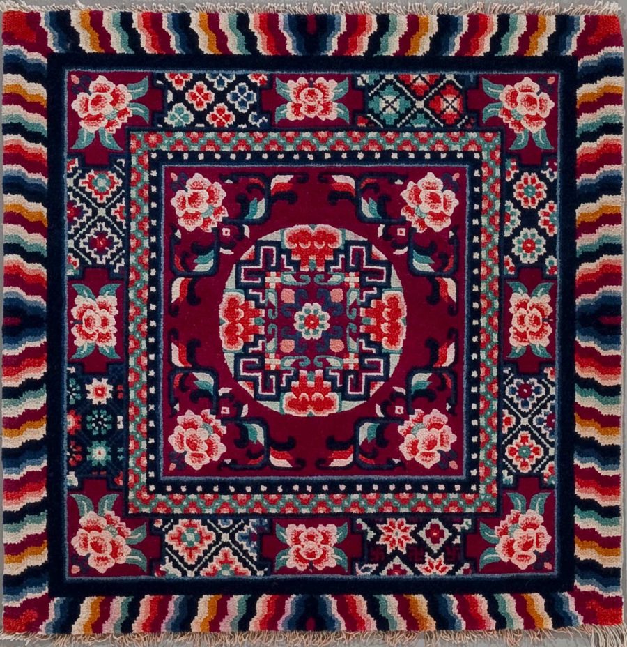 Traditioneller handgewebter Teppich mit einem zentralen geometrischen Muster in Rot und Blau, umgeben von floralen Motiven und einem vielfarbigen Wellenmuster als Rand.