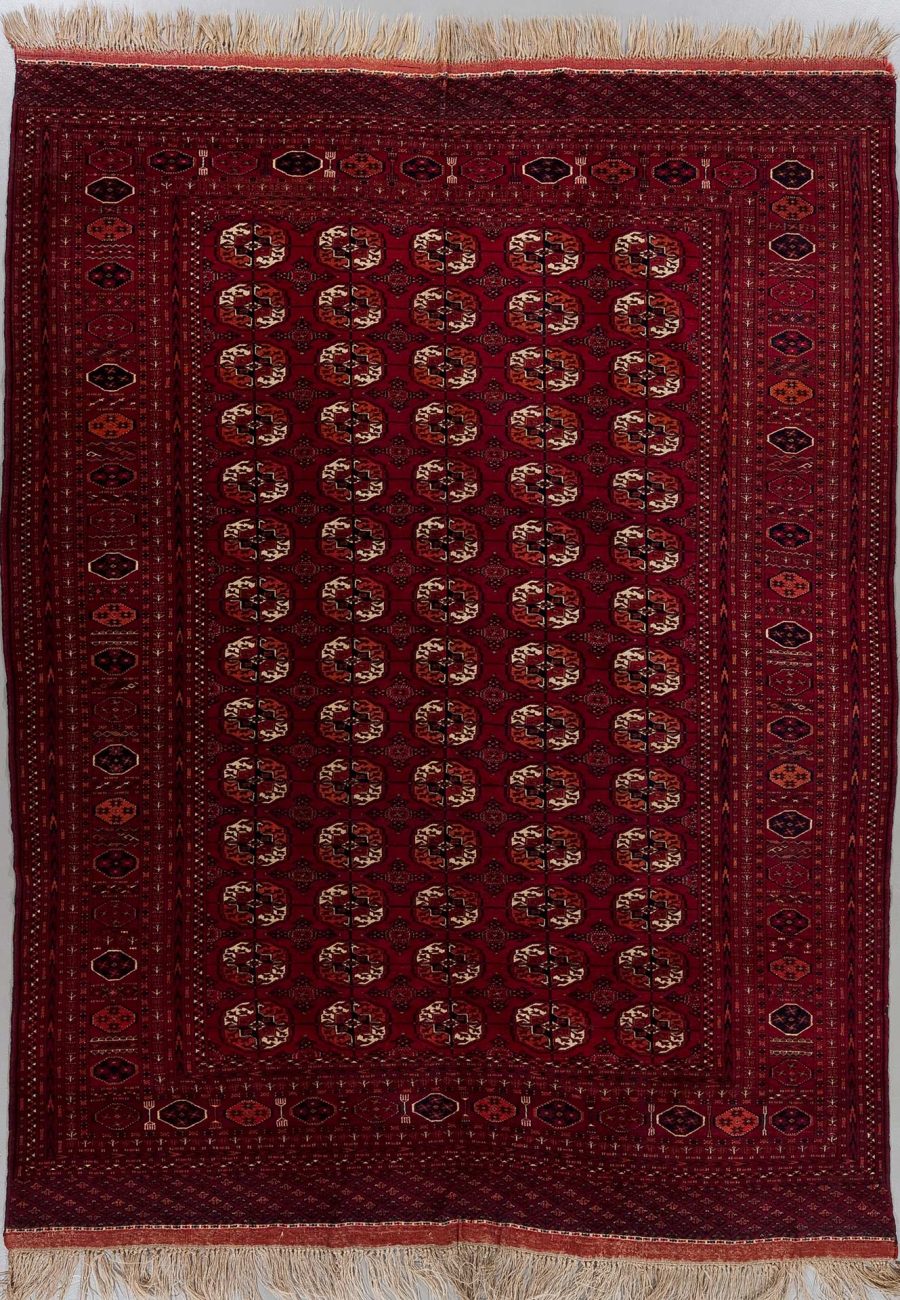 Detaillierter handgewebter orientalischer Teppich mit fransenbewehrten Enden, durchgehendem rotem Hintergrund und wiederkehrenden geometrischen und blumigen Mustern in Beige, Schwarz und Orange.