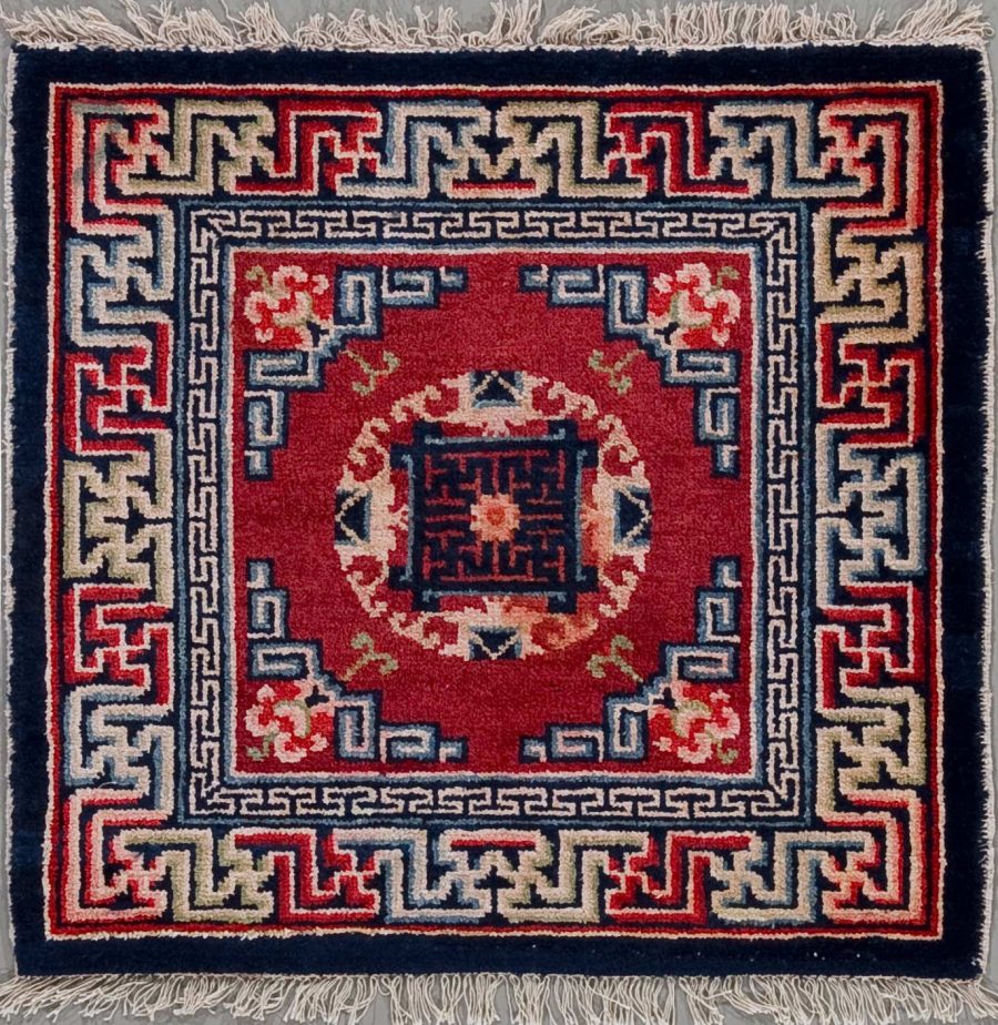Handgeknüpfter Teppich mit rotem zentralem Medaillon auf dunkelblauem Grund, umgeben von traditionellen geometrischen Mustern und Bordüren in den Farben Blau, Weiß und Beige, mit Fransen an den Enden.