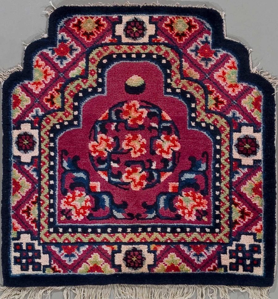 Detailaufnahme eines traditionellen Teppichs mit komplexem, symmetrischem Muster in Rot-, Blau- und Beigetönen mit floralen und geometrischen Formen, umgeben von einer Bordüre und Fransen an den kurzen Seiten.
