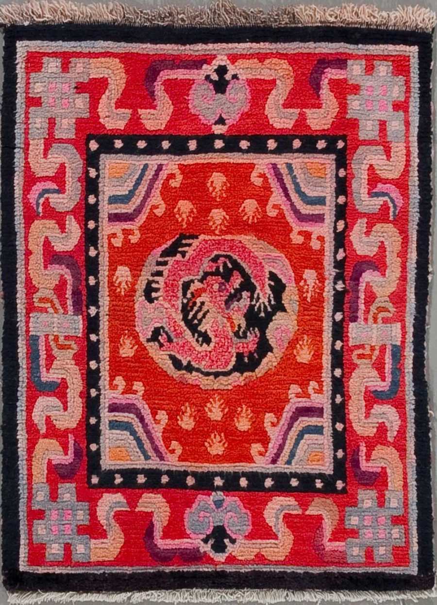 Quadratischer handgeknüpfter Teppich mit zentralem spiralförmigen Muster in Schwarz und Weiß auf rotem Hintergrund, umgeben von einem breiten, dekorativen Rahmen mit geometrischen und stilisierten floralen Motiven in Schwarz, Weiß, Blau und Pink.