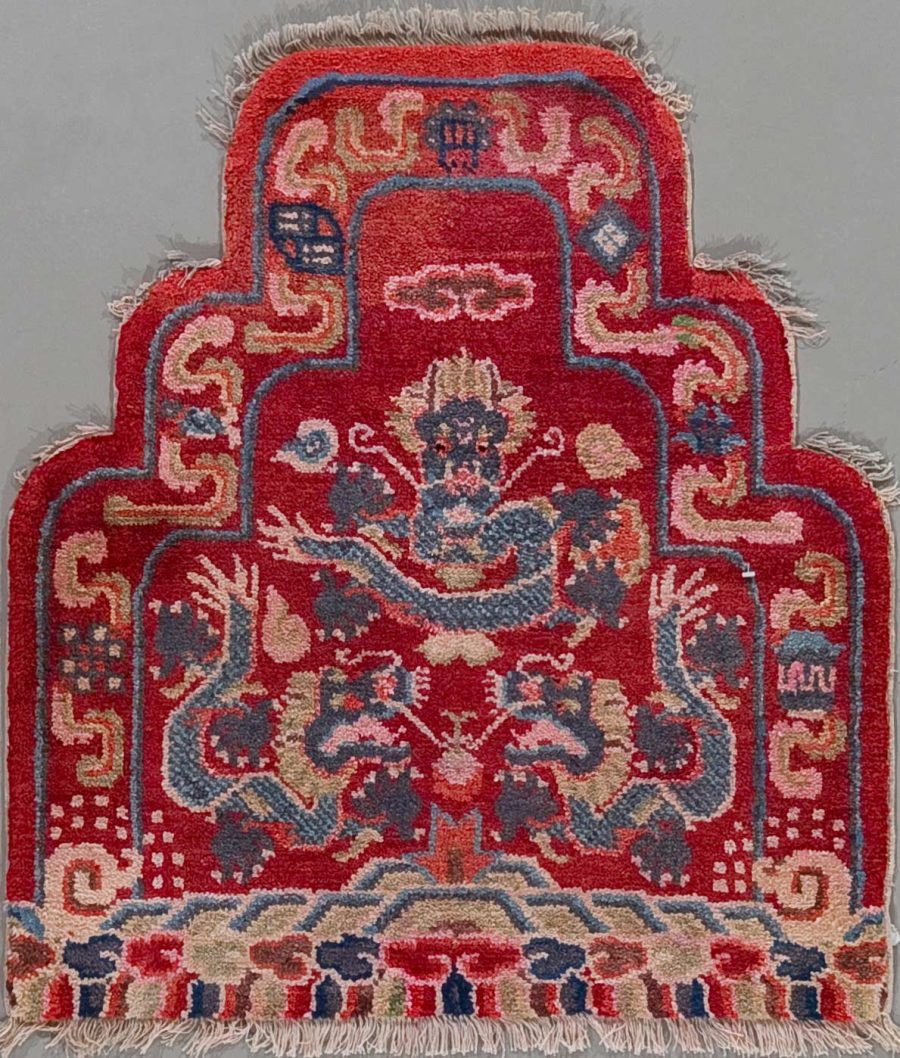 Traditioneller orientalischer Teppich mit aufwendigem Muster, hauptsächlich in Rottönen mit blauen, weißen und beige Akzenten, abgenutzte Kanten mit sichtbaren Fransen.
