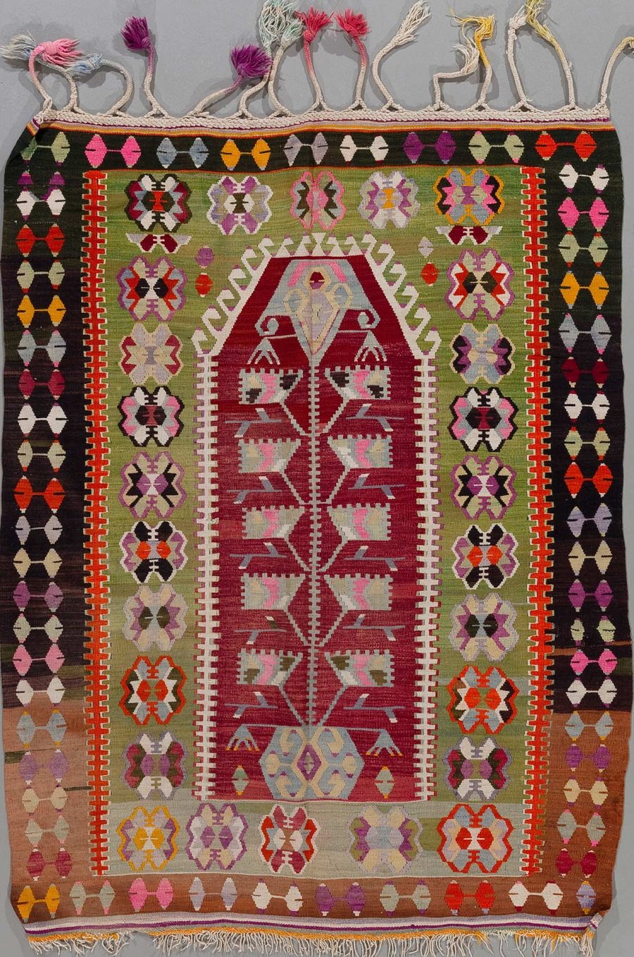Handgewebter Teppich mit bunten, geometrischen Mustern und Fransen an einem Ende.