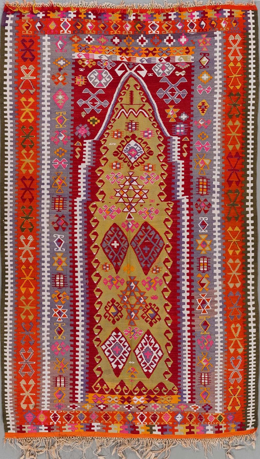 Traditioneller handgewebter Teppich mit reichhaltigen Mustern und einer zentralen Raute in Rot-, Gelb- und Orangetönen, flankiert von Vielfalt geometrischer und symbolhafter Designs in vielschichtigen Farben.
