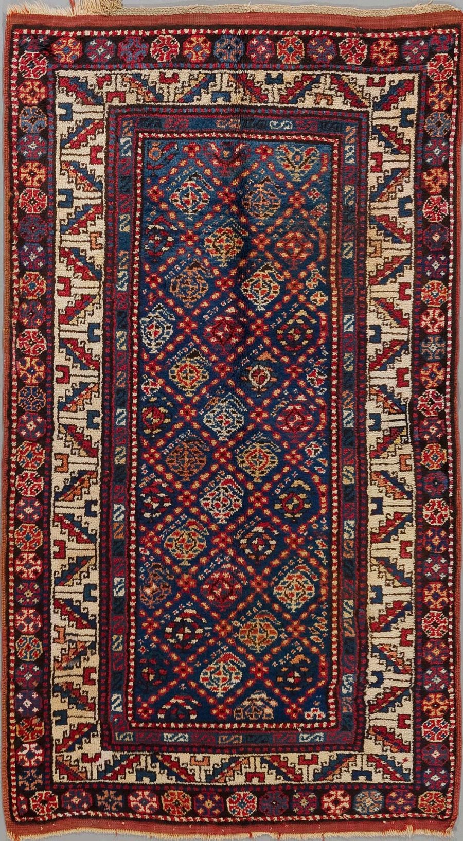 Alt-Text: Traditioneller orientalischer Teppich mit komplexem Muster in Blau, Rot und Beige, umgeben von mehreren verzierten Bordüren.