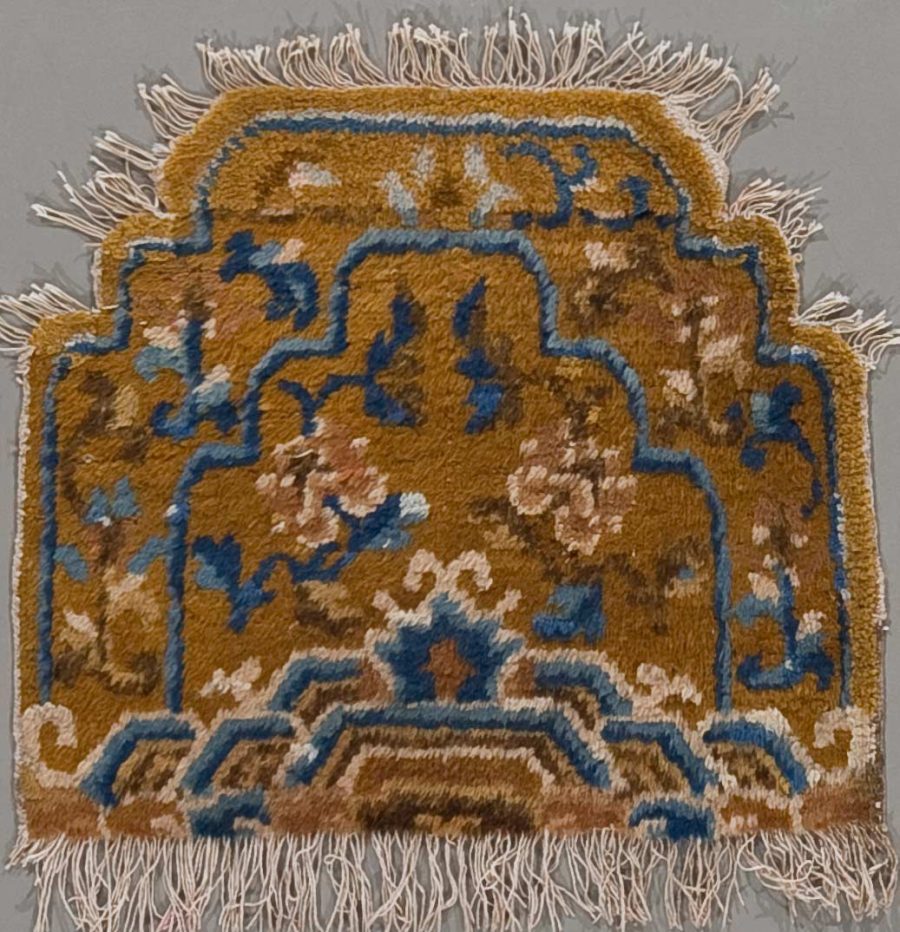 Detailaufnahme eines traditionellen Teppichs mit komplexen Mustern in Braun- und Blautönen mit Fransen an den Kanten.