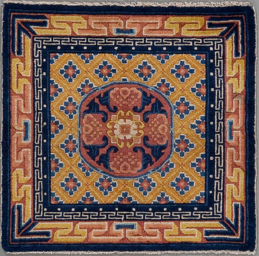 Quadratischer handgeknüpfter Teppich mit zentraler kreisförmiger Medaillon-Muster in Rot- und Beigetönen, umgeben von einem blau-orange gemusterten Feld und einer dunkelblauen Grenze mit griechischem Meandermuster.