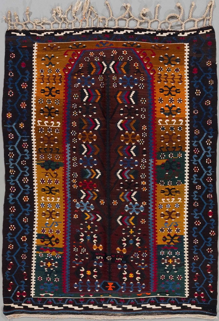 Handgewebter Teppich mit komplexen geometrischen Mustern und pflanzlichen Motiven in vielfältigen Farben auf dunklem Hintergrund, umrahmt von mehreren dekorativen Bordüren und versehen mit Fransen an den Enden.