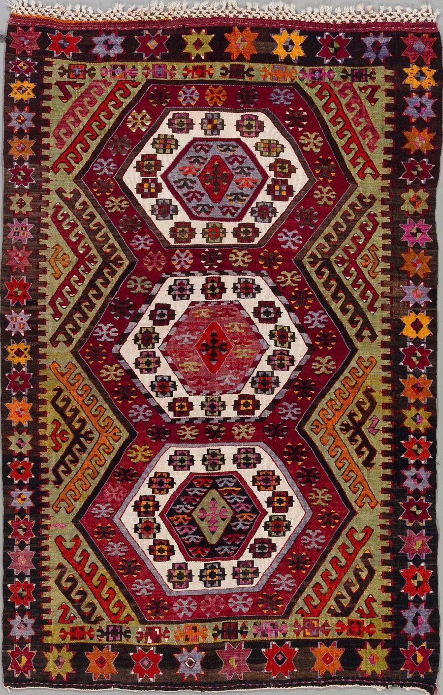 Handgewebter Teppich mit komplexen Mustern und reicher Farbpalette, bestehend aus zentralen Diamanten und umgebenden geometrischen und floralen Motiven in Rot-, Schwarz-, Grün- und Gelbtönen.