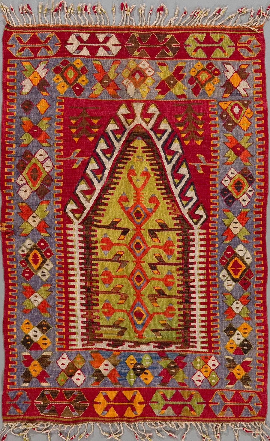 Traditioneller handgewebter Teppich mit komplexem Muster aus geometrischen Formen und Symmetrien in lebendigen Farben, darunter Rot, Blau, Gelb und Grün, mit ausgefransten Kanten an den Enden.