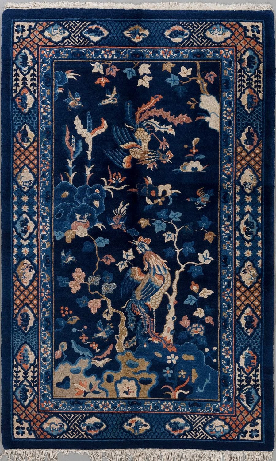 Traditioneller, handgeknüpfter Teppich mit einem dunkelblauen Hintergrund und einem detaillierten floralem und tierischem Muster, einschließlich Pfauen und verschiedenen Blumenarten, umgeben von einer dekorativen Bordüre mit geometrischen und floralen Elementen, komplettiert durch einen Fransenabschluss.